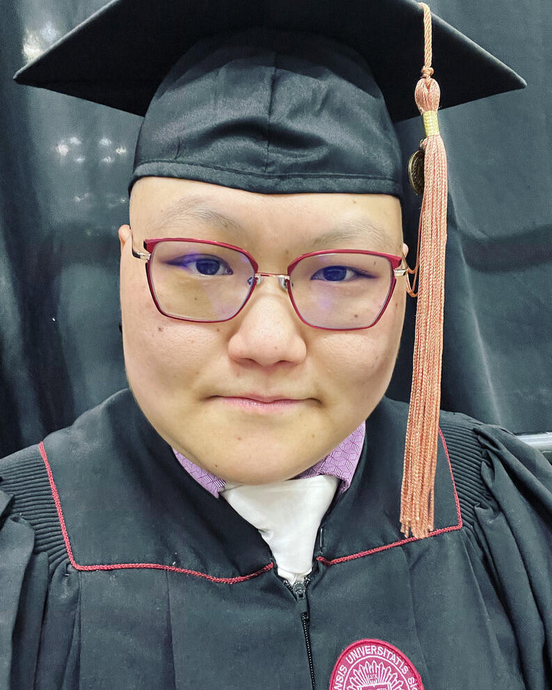Image of a person in graduation garb looking straight at the camera.